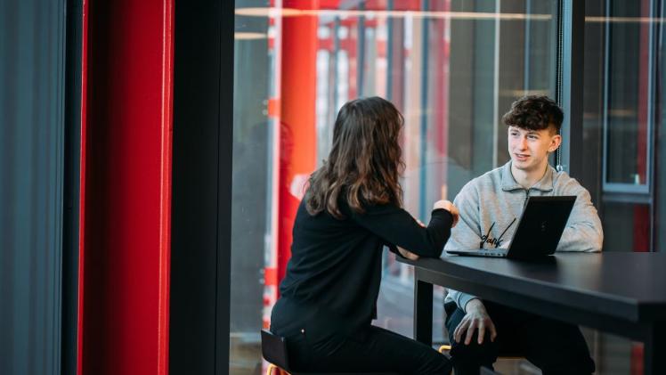 student sitting at a table speaking to a Queen's staff member